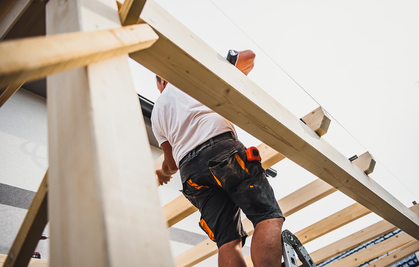 Aufbau der Holzstruktur der neuen Terrassenüberdachung – Stabilität sichern Handwerker auf Leiter befestigt Holzbalken für die Terrassenüberdachung.