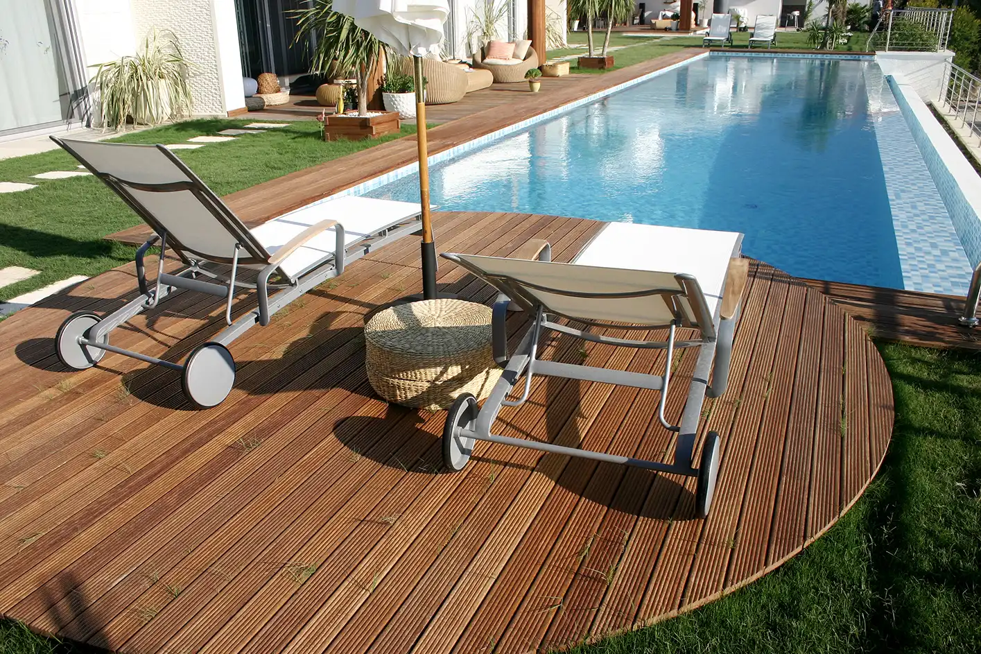 Holzterrasse als Poolumrandung mit Sonnenliegen im modernen Garten