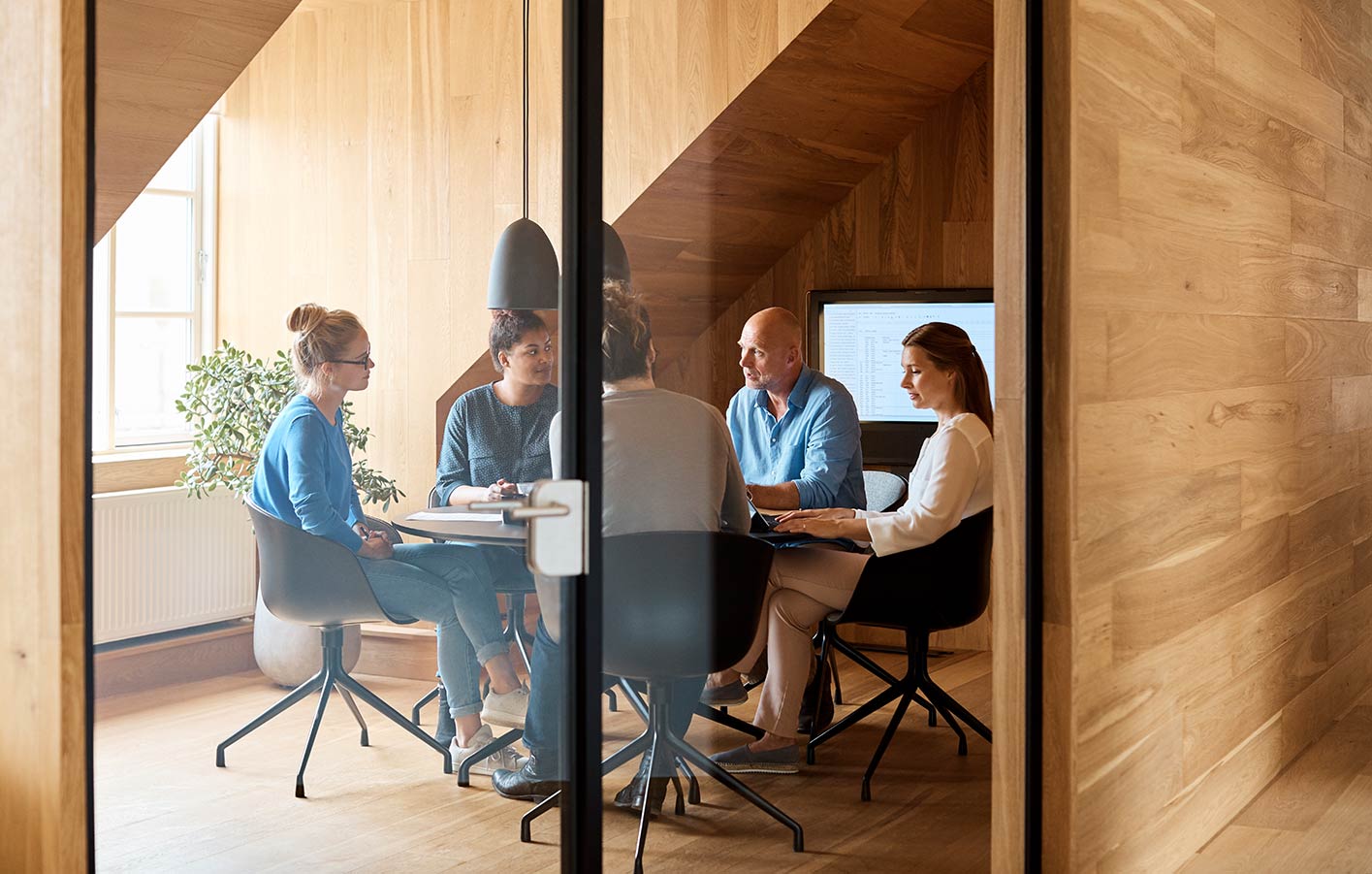 Glastür - dahinter sieht man ein Konferenzraum mit Menschen, die sich in einem Meeting befinden